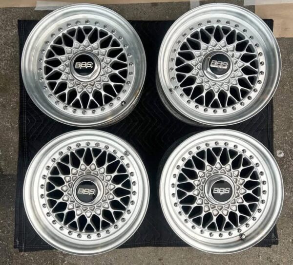 BBS RS three-piece forged split rim wheels featuring a raw silver finish, iconic cross-spoke pattern, polished stepped lips, and original black center caps with chrome BBS lettering