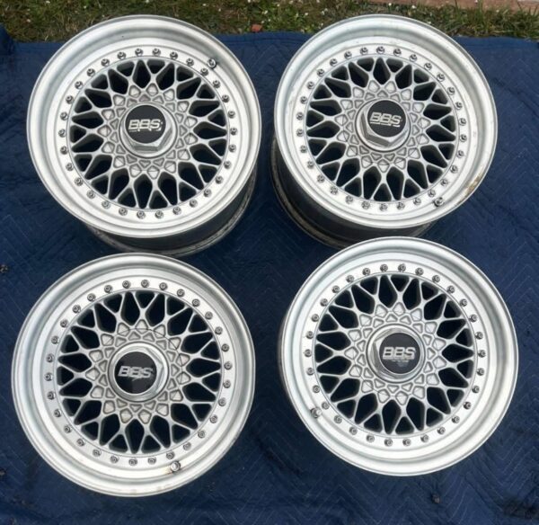 BBS RS three-piece forged split rim wheels featuring a raw silver finish, iconic cross-spoke pattern, polished stepped lips, and original black center caps with chrome BBS lettering