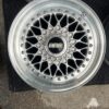 BBS RS three-piece forged split rim wheels featuring a raw silver finish, iconic cross-spoke pattern, polished stepped lips, and original black center caps with chrome BBS lettering