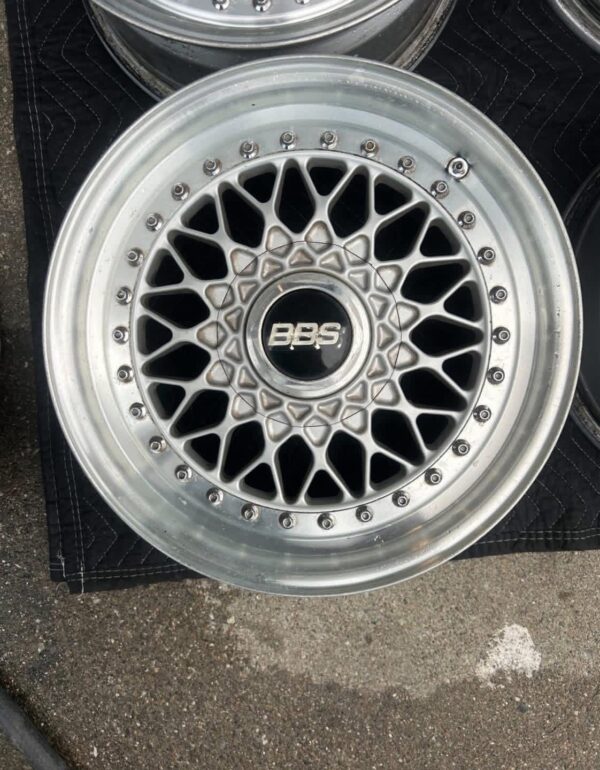 BBS RS three-piece forged split rim wheels featuring a raw silver finish, iconic cross-spoke pattern, polished stepped lips, and original black center caps with chrome BBS lettering