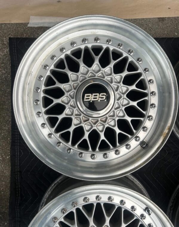 BBS RS three-piece forged split rim wheels featuring a raw silver finish, iconic cross-spoke pattern, polished stepped lips, and original black center caps with chrome BBS lettering