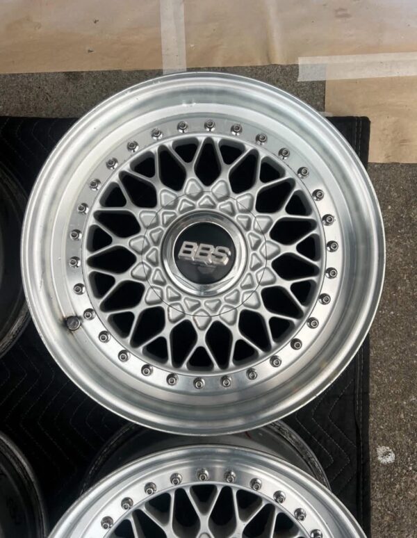 BBS RS three-piece forged split rim wheels featuring a raw silver finish, iconic cross-spoke pattern, polished stepped lips, and original black center caps with chrome BBS lettering