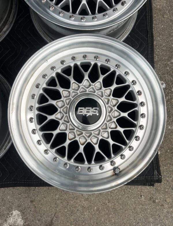 BBS RS three-piece forged split rim wheels featuring a raw silver finish, iconic cross-spoke pattern, polished stepped lips, and original black center caps with chrome BBS lettering